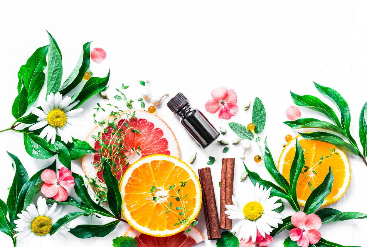 Bottles of essential oil, lemons, flowers, and cinnamon sticks scattered on a white background