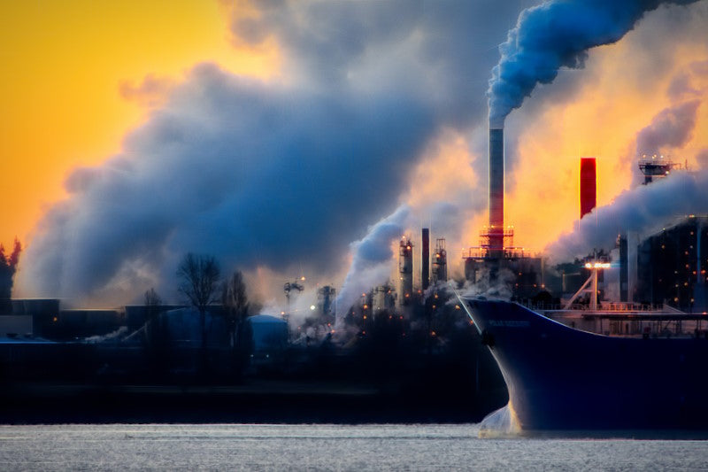 Ship passing through water with a smoky factory in the background