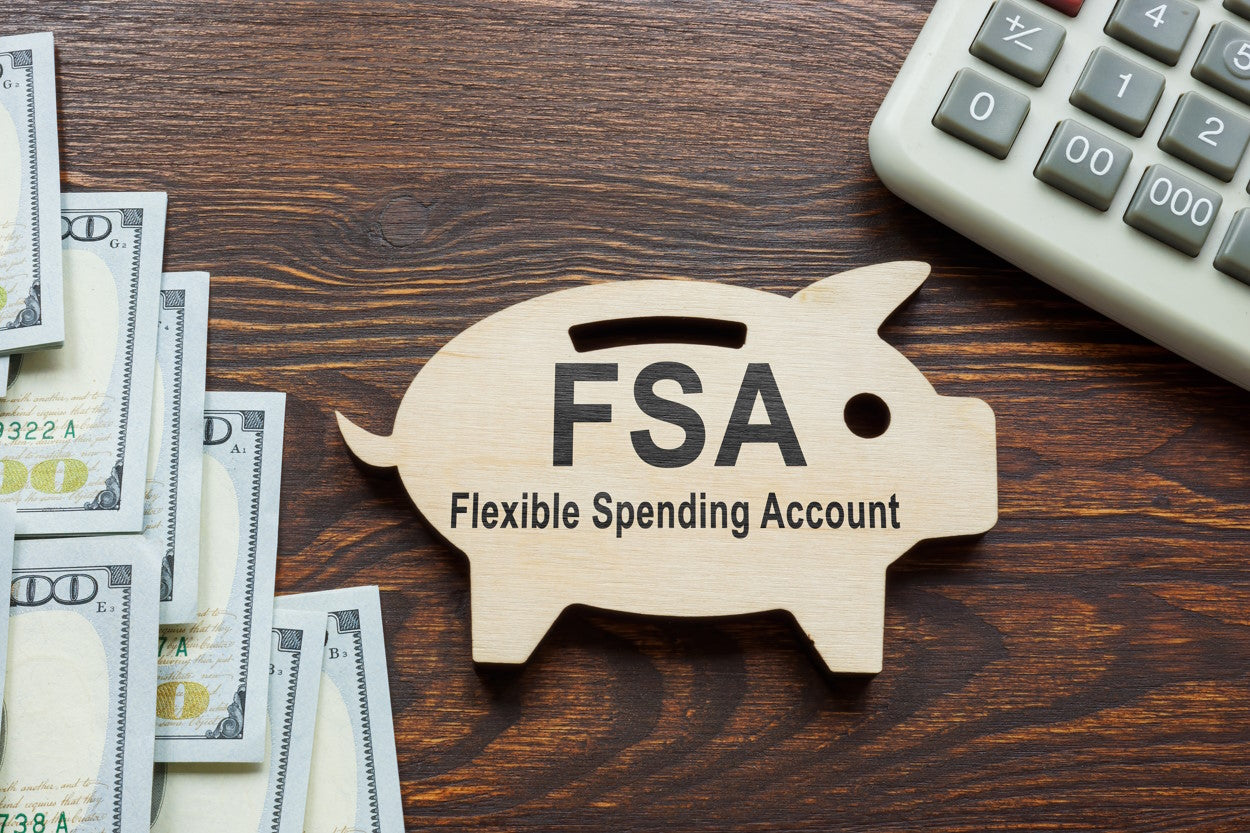 Desk with calculator, cash, and a wooden piggy bank labeled 'FSA Flexible Spending Account'