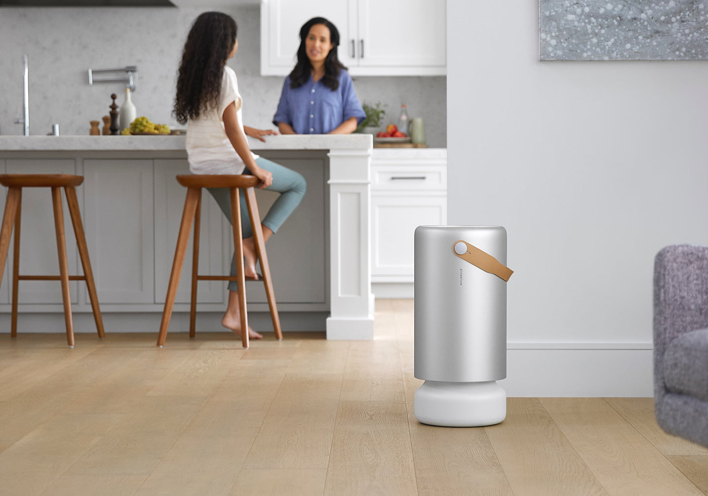 Young girl sitting on kitchen stool and talking to mother with a Molekule Air Pro air purifier in foreground