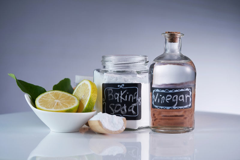 Bottles of baking soda and vinegar next to a bowl of sliced lemons