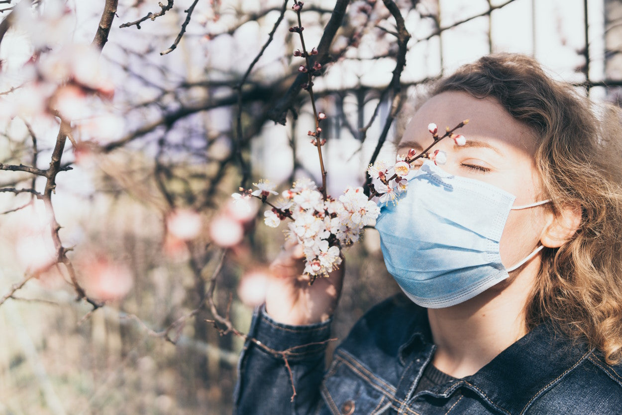 Woman wearing a face mask and smelling tree blossoms