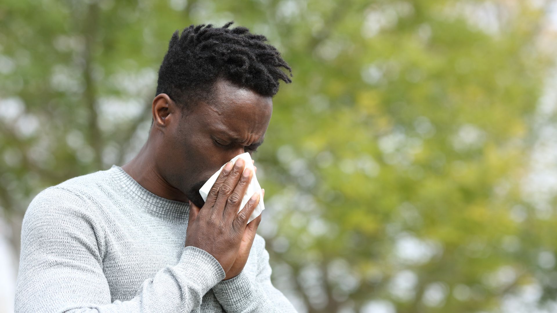 Man blowing his nose outdoors