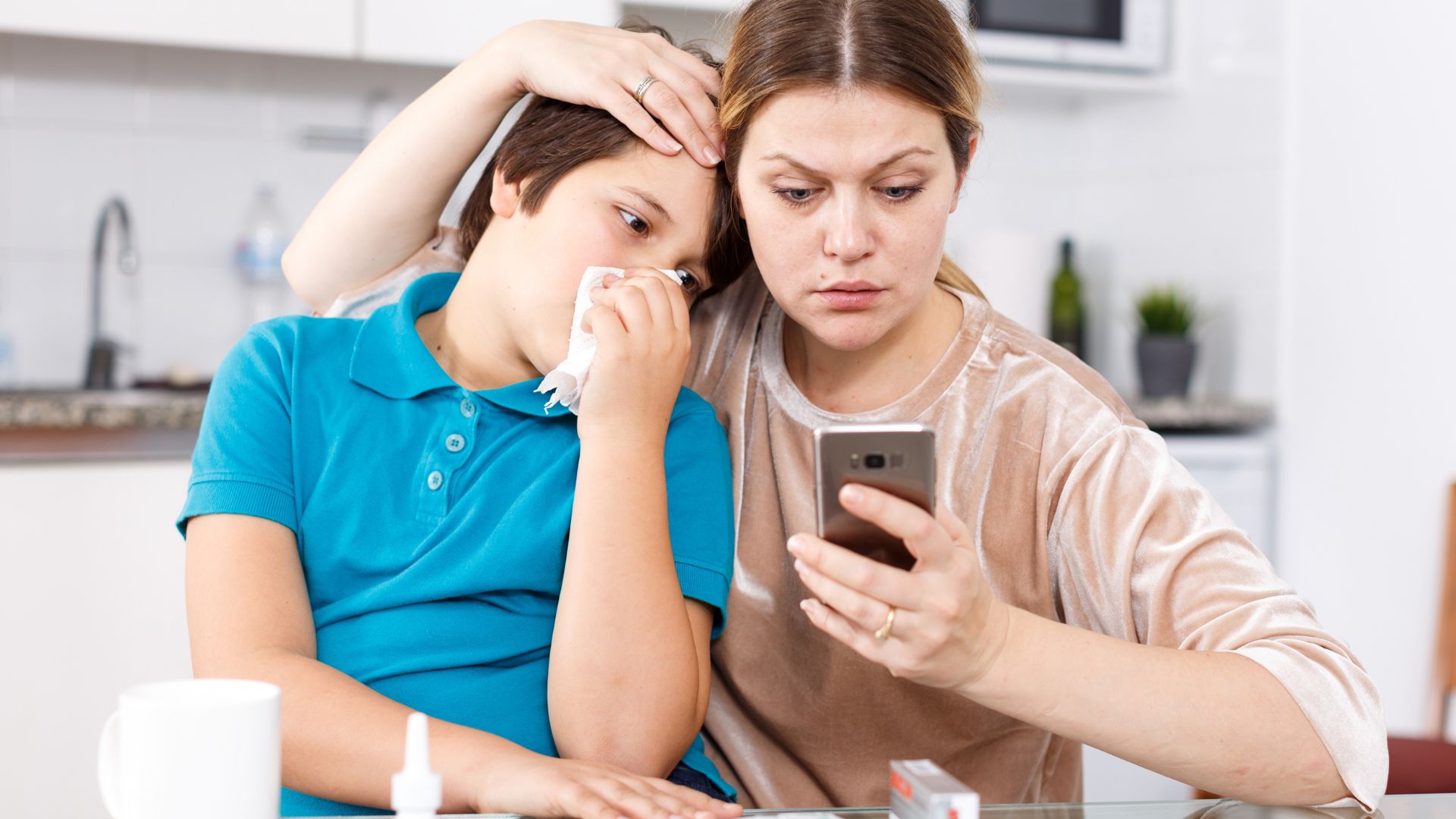 Mother comforting son with allergies as she looks for allergy information on her phone