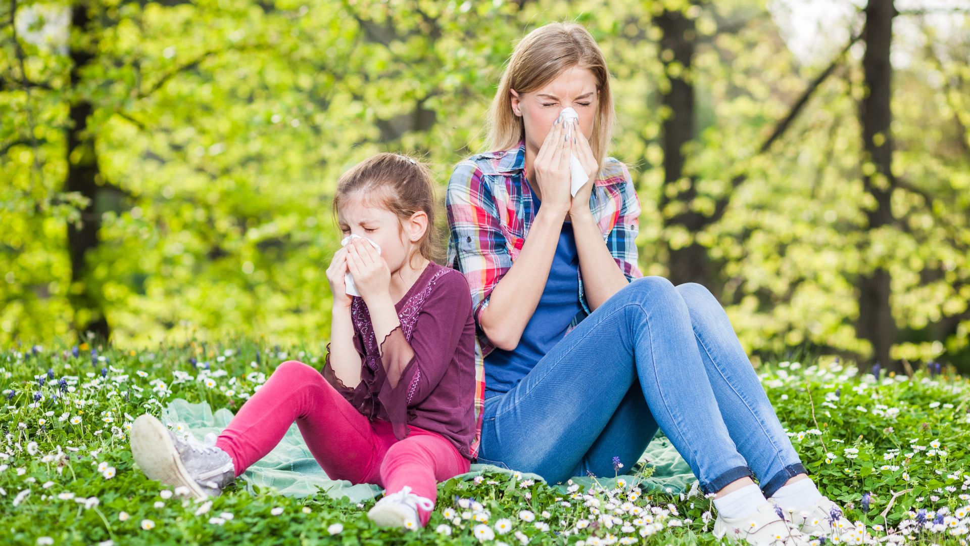 Mother and daughter blowing their noses in a green field