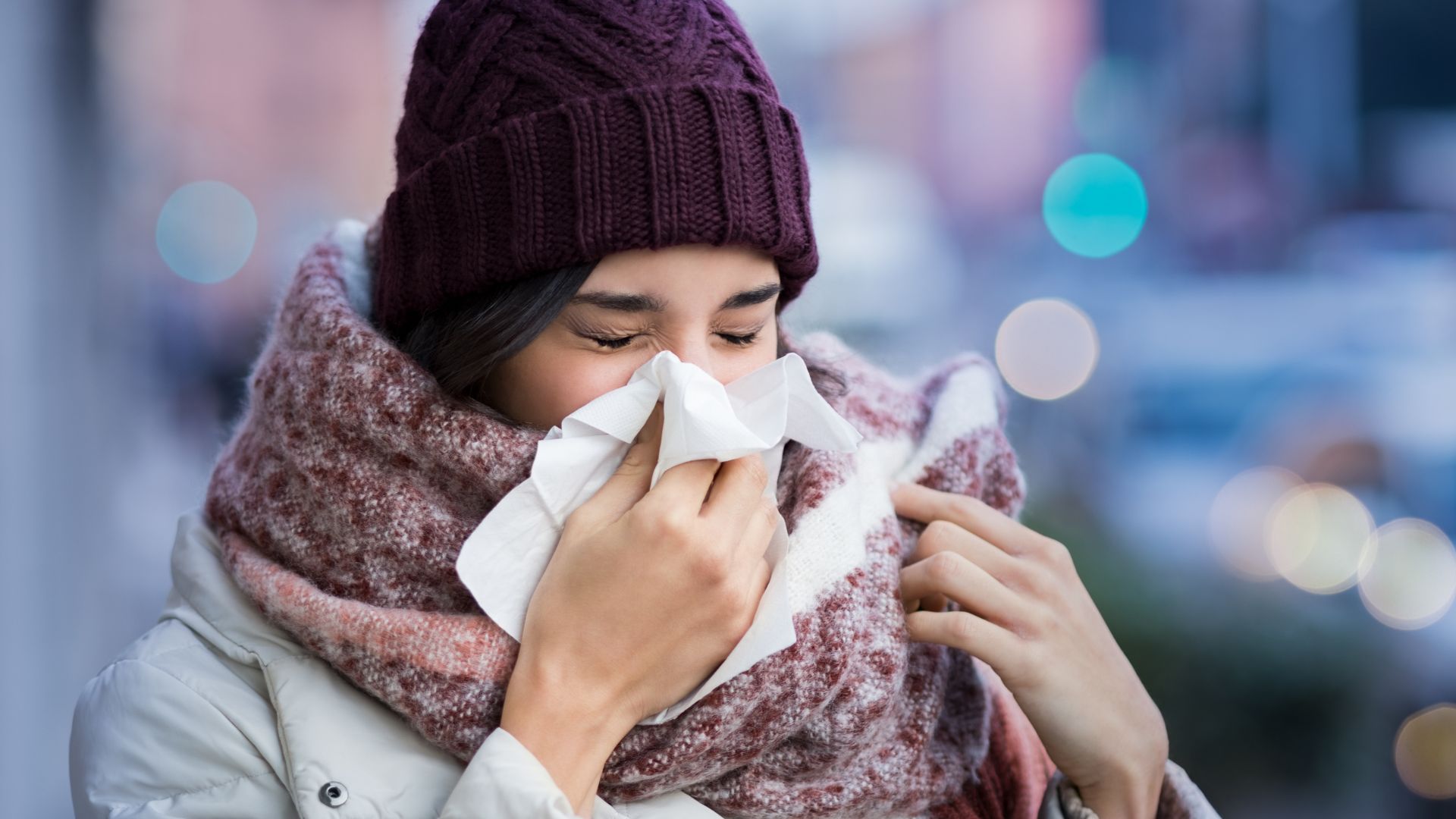 Woman in scarf and hat blowing her nose