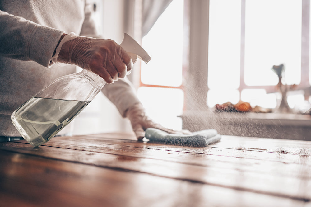 Gloved hand spraying cleaning product onto wood table surface